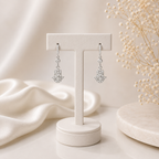 Silver hamsa hand earrings on a white stand with a soft beige background