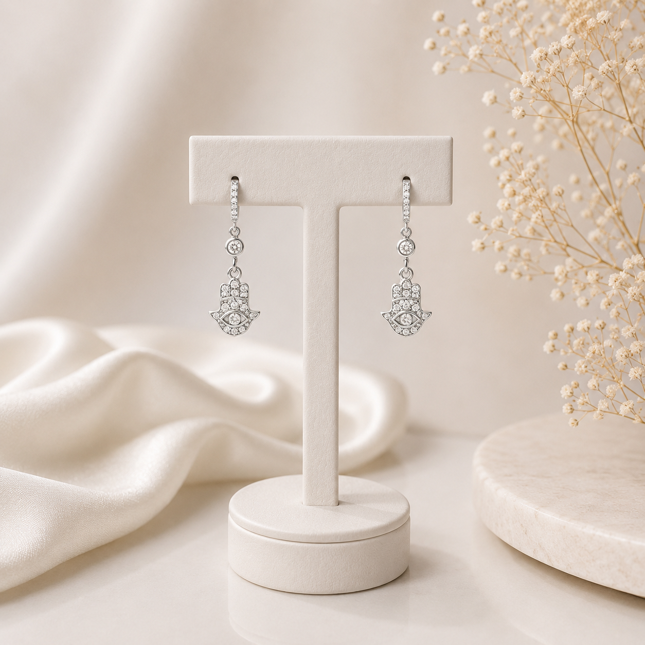 Silver hamsa hand earrings on a white stand with a soft beige background