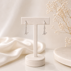 Silver earrings on a white jewelry stand with a soft beige background
