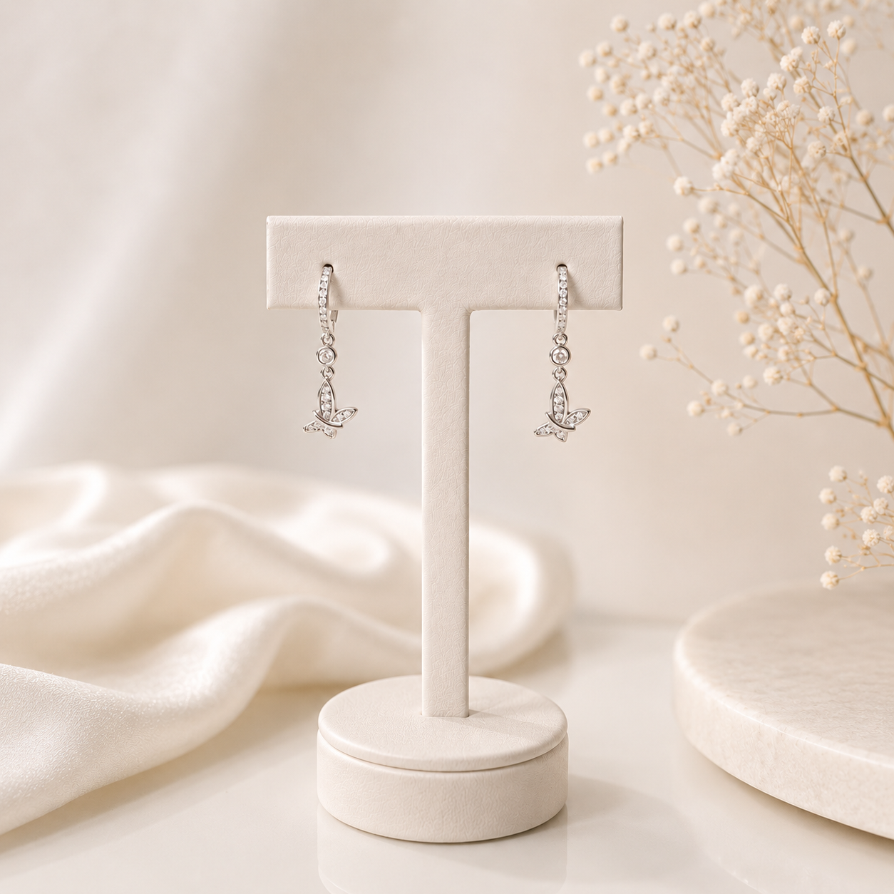 Silver earrings on a white jewelry stand with a soft beige background